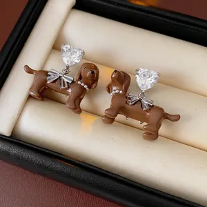 Cute dachshund puppy earrings with heart-shaped gems and silver bow details in a jewelry box