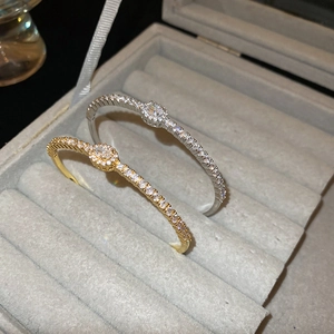 Detail view of gold and silver plated bangles with oval zircon stones on grey velvet box