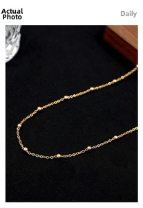 Detailed macro view of a golden stainless steel bead chain necklace on a black textured background
