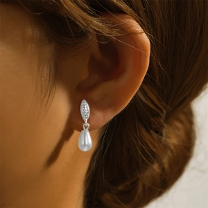 Detail of silver olive leaf stud earrings with white teardrop pearls on a model