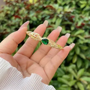 Detail of 18K gold-plated open bangle featuring pear-cut emerald and hollow geometric patterns