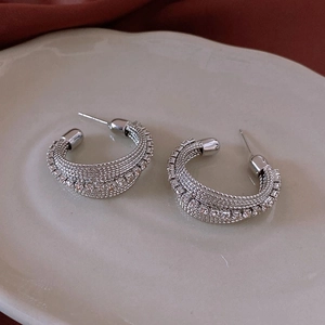 Macro shot of silver C-shaped woven earrings with sparkling rhinestones on ceramic tray