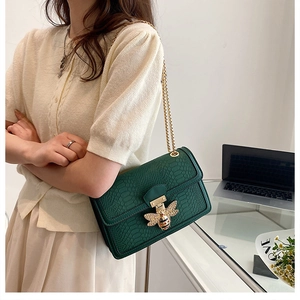 Detail of dark green snake-embossed crossbody bag with golden bee buckle and chain strap