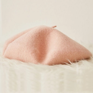 Fashionable pink wool beret with soft fiber texture on a plush white surface