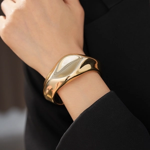 Close-up of a wide golden cuff bracelet with irregular fluid shapes on a model arm
