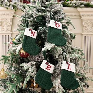 Green knitted Christmas stockings with NOEL red embroidery hanging on a snowy Xmas tree