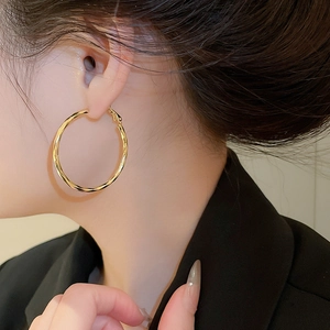 Close-up of a model wearing large 14k gold plated twisted hoop earrings with glossy finish