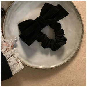 Detail of a black velvet bow scrunchie on a white ceramic plate with beige linen background