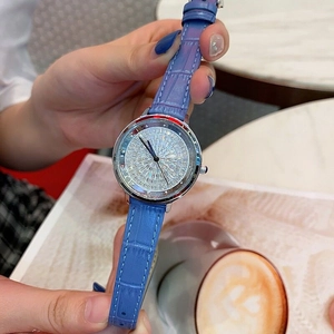 Close-up of a women's watch with blue leather strap and full diamond dial on a coffee table
