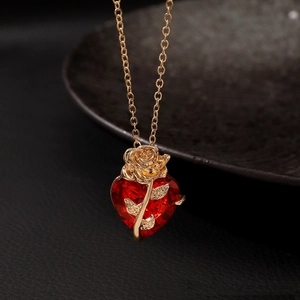 Close-up of gold chain necklace featuring a red heart pendant with a gold rose detail