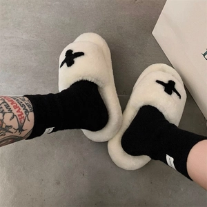 Close-up of thick plush slippers with black cross embroidery and soft white faux fur