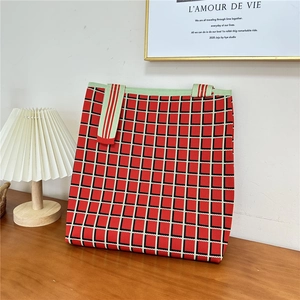 Close-up of red and black checkered knit tote bag with striped straps on wooden table