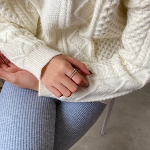 Close-up of gold and silver irregular bubble texture rings worn with a knit sweater