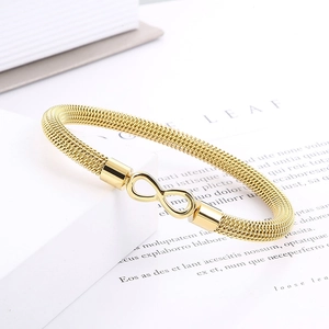 Macro detail of gold mesh bracelet featuring a polished infinity symbol on a white background