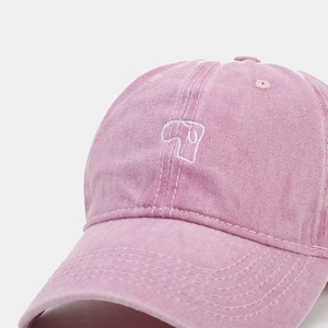 Detail of pink washed cotton baseball cap featuring white abstract embroidery on front