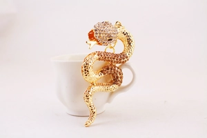 Detailed view of a gold-tone snake keychain with sparkling rhinestones on a white cup