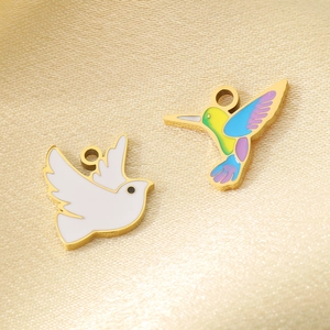 Detail of colorful hummingbird and white dove enamel charms on golden silk background