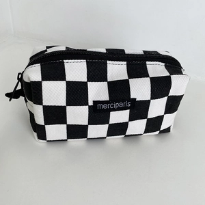Close-up of a checkered canvas pencil case featuring a black brand tag with zipper detail