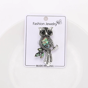 Detail of owl brooch with colorful abalone shell inlays on a white jewelry dish