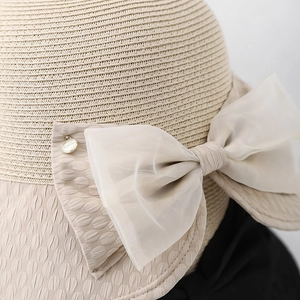 Close-up of the beige straw sun hat featuring a layered organza bow and gold HER metal button