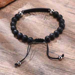 Verstellbares Herrenarmband mit matten Onyxperlen und gravierbarer Metallplatte auf Holzgrund