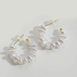 Detail of C-shaped hoop earrings featuring white baroque pearls and golden metal finish