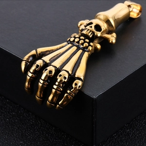 Golden vintage ghost claw hand pendant in titanium steel with skull detail on black surface