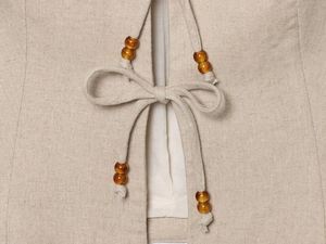 Close-up of beige linen vest with beaded drawstring ties and natural woven fabric texture
