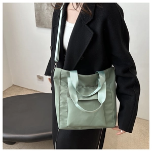 Close-up of light green nylon tote bag featuring wide shoulder straps and a front flap pocket