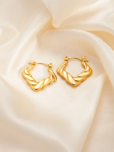 Close-up of golden twisted hoop earrings on silk background highlighting premium texture