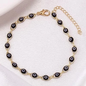 Macro detail of gold evil eye bracelet with lobster clasp on white silk fabric