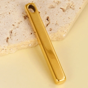 Macro shot of a polished gold rectangular stainless steel pendant on a beige stone base