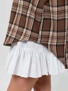 Close-up of brown plaid shirt with white ruffled skirt showing fabric texture and layers