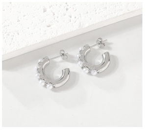 Detail of silver C-shaped stainless steel earrings inlaid with white pearls on stone background