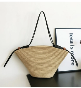 Detail of woven tote bag featuring black shoulder straps and decorative wooden beads