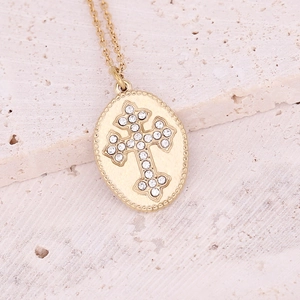 Macro detail of gold oval cross pendant with cubic zirconia on textured stone
