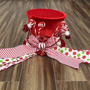 Detail view of red velvet Christmas tree topper hat with striped ribbons and faux candies