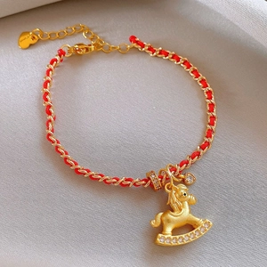 Close-up of golden rocking horse charm with zircon stones and red braided cord