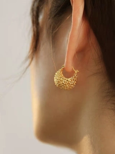 Macro detail of gold-tone woven hollow ball earrings showing luxurious metal texture