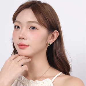 Close-up of heart-shaped gold-rimmed earrings with black inlay worn by a model