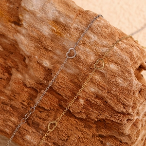 Macro shot of 14K gold and silver heart link chains on a natural rustic wood background