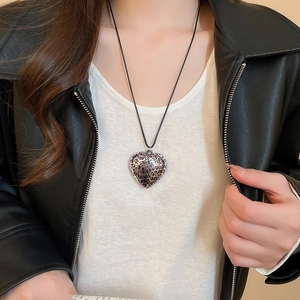 Detail of a leopard print heart pendant necklace worn with a stylish leather jacket