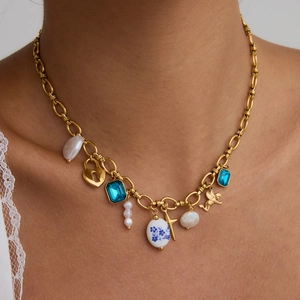 Detail of gold chain necklace with baroque pearl, blue gemstone, and ceramic charms