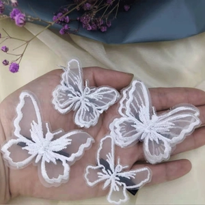 Detail of four white embroidered butterfly hair clips showing size scale in hand