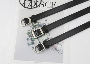 Detailed view of three black faux leather belts with square and D-shaped silver buckles