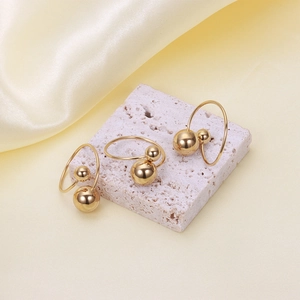 Detailed view of three gold 18K stainless steel ball rings on a white stone display stand