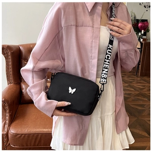 Detail of black nylon crossbody bag featuring silver butterfly and wide logo strap