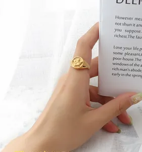 Detailed close-up of a gold-plated signet ring with an embossed angel motif on a finger