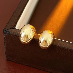 Close-up of gold oval mirror earrings on a dark wooden jewelry box with high-gloss finish