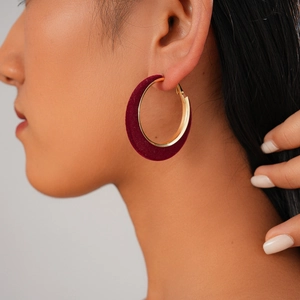 Close-up of burgundy flocked C-hoop earring with gold-tone metal trim on a female model